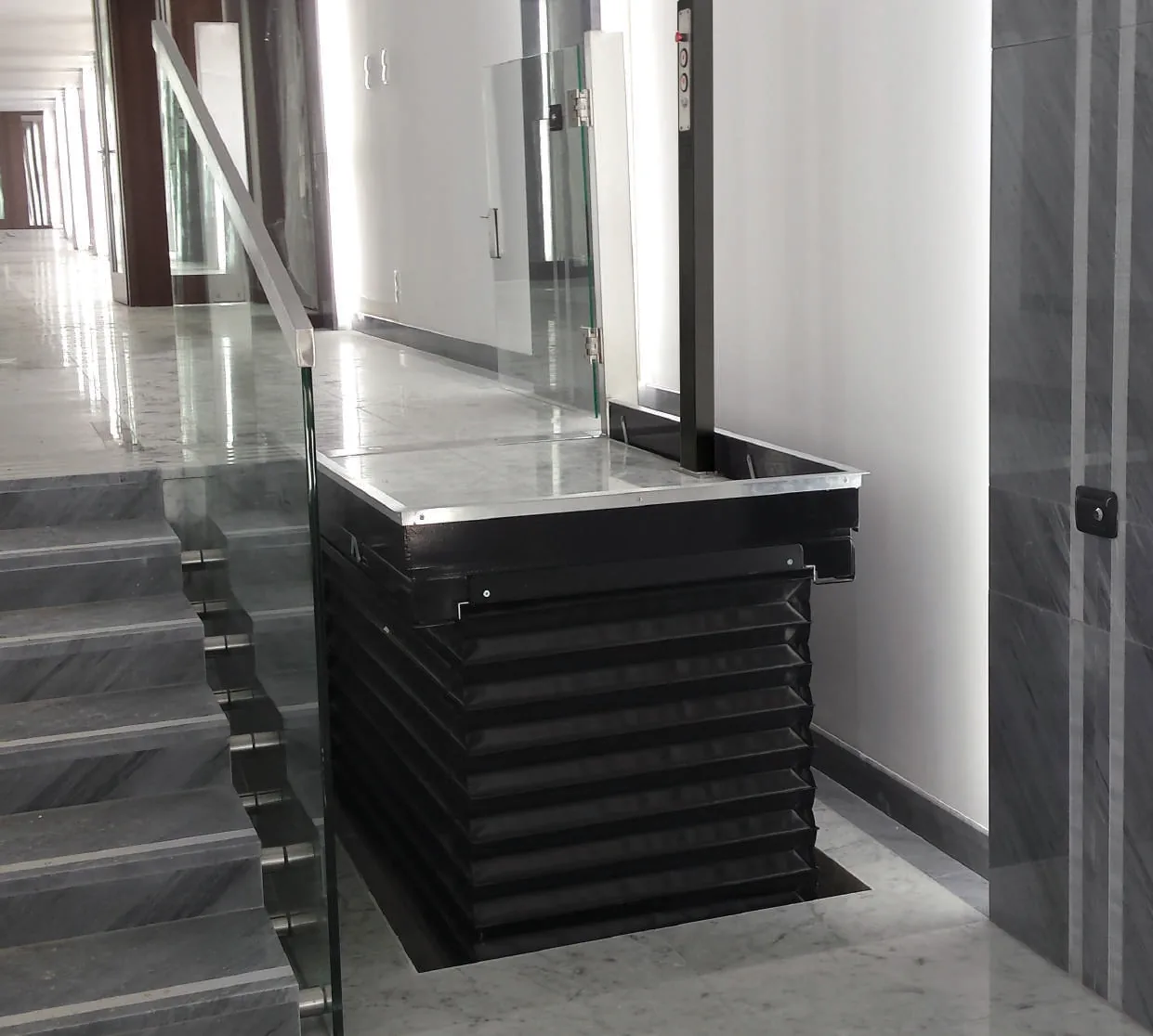Élévateur vertical avec soufflet noir déployé dans un couloir moderne en marbre blanc