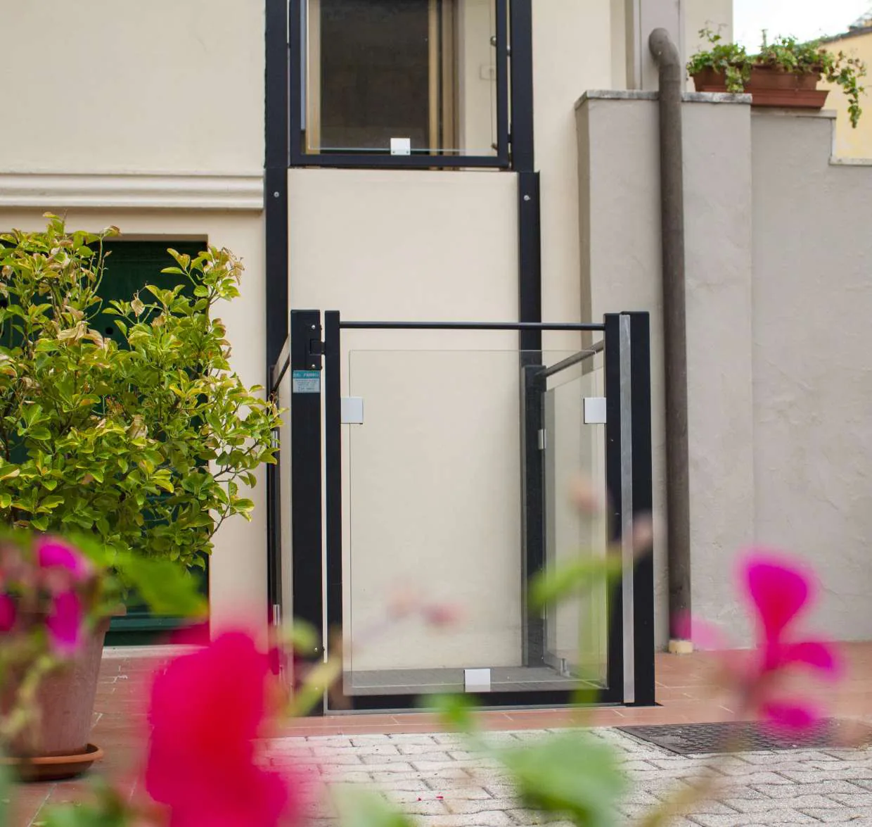 Plateforme élévatrice verticale extérieure avec parois vitrées et structure noire, contre une façade claire